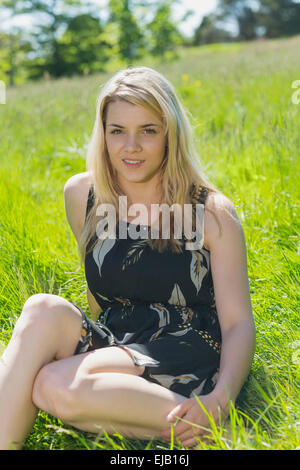 Pretty blonde in sundress sitting on grass Stock Photo - Alamy