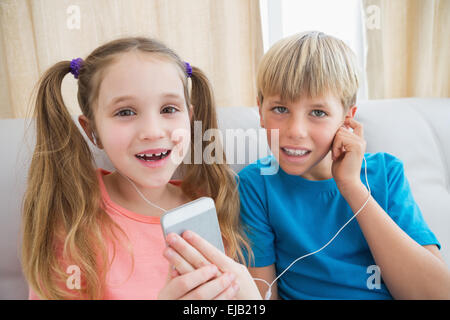 Happy siblings listening to music on sofa Stock Photo