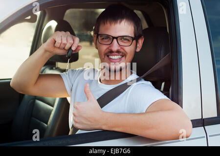 Young male european driver is holding new car key and showing thumb up Stock Photo