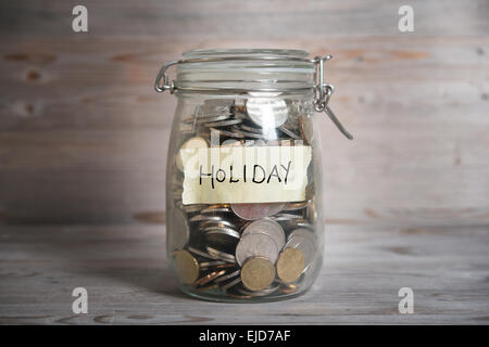 Coins in glass money jar with holiday label, financial concept. Vintage wooden background with dramatic light. Stock Photo