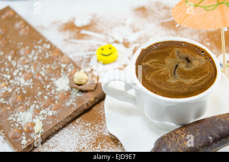 White cup full with deliciously looking coffee and whole nut chocolate in the background decorated with a paper umbrella Stock Photo
