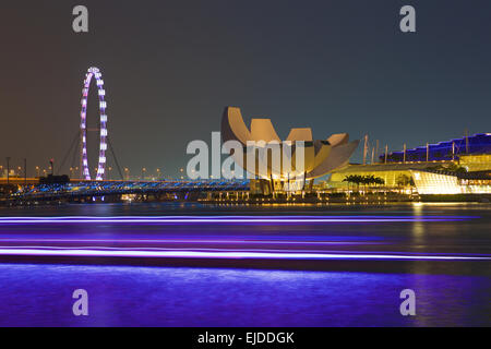 Light Trails From Passing River Tour Boats On Marina Bay At Night, Singapore. Stock Photo