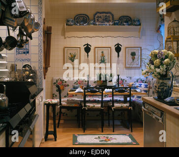 Pictures on wall above floral banquette seating in dining area of nineties kitchen Stock Photo