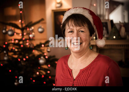 A woman by a Christmas tree wearing a Santa hat. Stock Photo