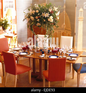 Large summer flower arrangement on table set for lunch in nineties dining room with upholstered chairs Stock Photo