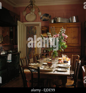 Bentwood chairs at simple pine table set for lunch in nineties kitchen with an Aga oven and pine cupboard Stock Photo