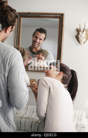 A mother and father with their baby, looking in the mirror. Stock Photo