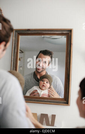 A mother and father with their baby, looking in the mirror. Stock Photo