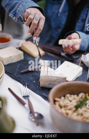 A woman using a knife to cut cheese on a slate board. Stock Photo