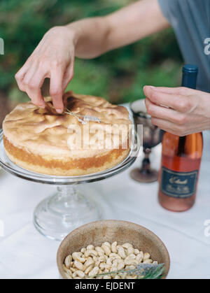A woman decorating a cake on a glass stand. A dish of nuts and a bottle of rose wine. Stock Photo
