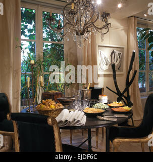 Black+gilt chairs at table set for lunch in nineties dining room with antique Venetian glass chandelier Stock Photo