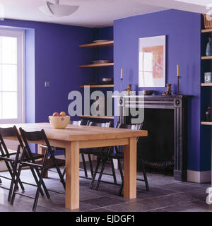 Black folding chairs at simple wood table in bright blue dining room with slate fireplace and tiled floor Stock Photo