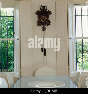 Vintage cuckoo clock on wall between windows in white dining room Stock Photo