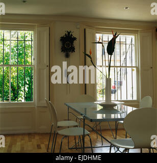 White Arne Jacobsen style chairs at glass topped table in modern dining room with vintage cuckoo clock on wall Stock Photo