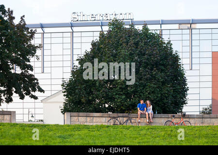 Young couple sitting on wall with their bikes in front of Sheraton Hotel in the evening light at Krakow, Poland in September Stock Photo