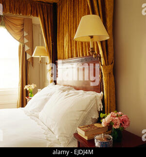 Yellow lamps fitted on four poster bed with yellow drapes and white pillows in traditional townhouse bedroom Stock Photo