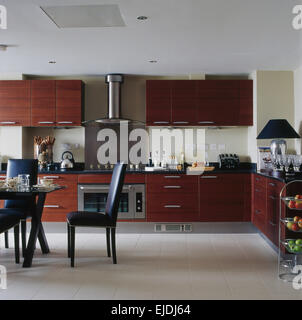 White ceramic tiled floor in modern kitchen with dark brown wood cupboards and black leather dining chairs Stock Photo