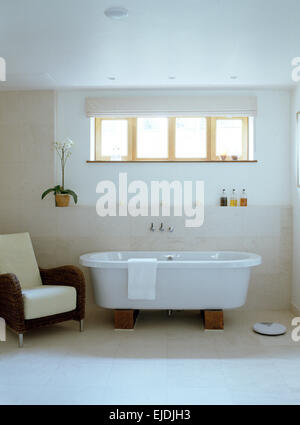 Modern roll top bath in white contemporary bathroom with wicker armchair Stock Photo