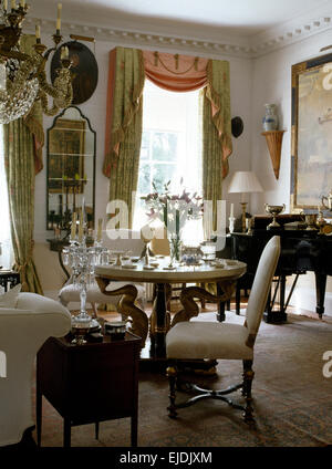 White upholstered chairs at ornate table in traditional dining room with green silk swagged+tailed curtains Stock Photo