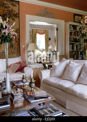 White sofas in traditional peach sitting room with pink lilies in a tall glass vase on the coffee table Stock Photo