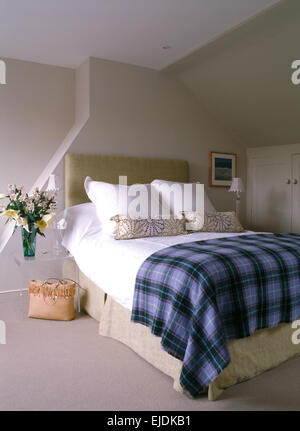 Folded blue plaid rug on upholstered bed with white pillows in pale gray modern bedroom Stock Photo