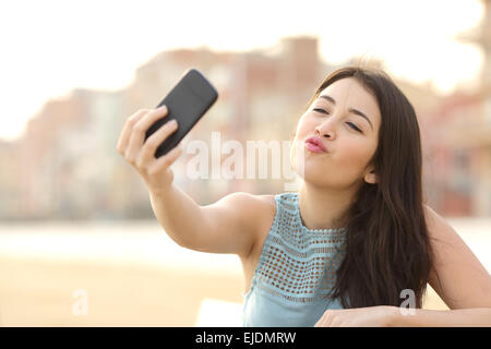 Teen girl photographing a selfie kissing camera with a smart phone in an urban park Stock Photo