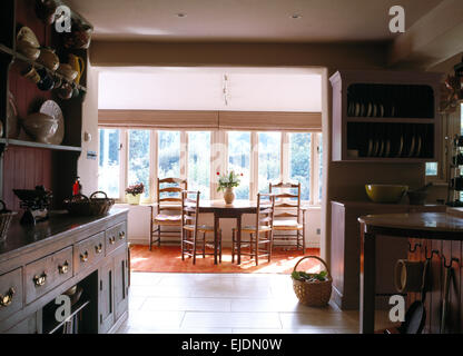 Open-plan country kitchen and dining room with antique ladder back chairs at small table in front of the window Stock Photo