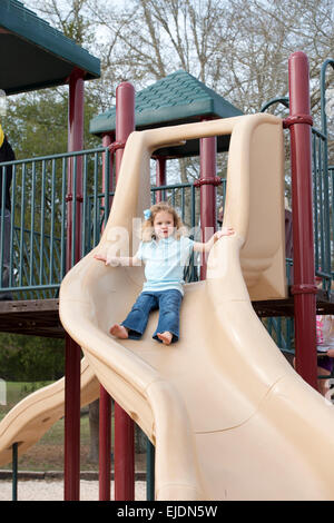 Young girl goes down slide at park playground Stock Photo