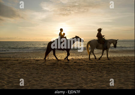A woman and he child are led by a man on a beach horseback ride
