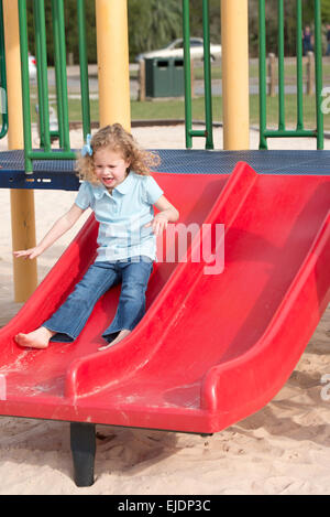 Four year old girl goes down slide at park playground Stock Photo