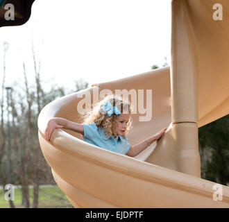 Four year old girl going down slide at park playground Stock Photo