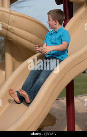 Eight year old boy sliding at park playground Stock Photo