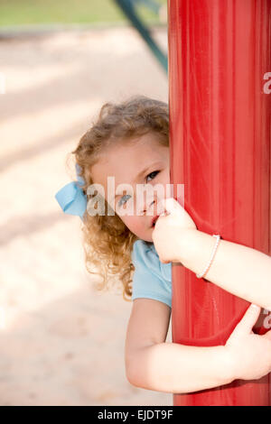 Four year old girl playing at park playground and hugging a red pole Stock Photo