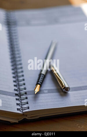 Closeup photo of open notebook with a fountain pen, placed at wood background. Stock Photo