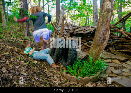 A girl jumps over a boy at their make shift hut in the woods at Pittsburgh PA. during the spring Stock Photo