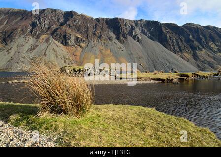 wastwater screes on a sunny bright winters evening with blue sky and white clouds and grass and lake in the foreground Stock Photo