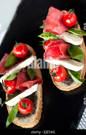 Toasts with tomato, ham, basil and eggplant puree Stock Photo