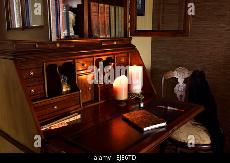 Classic wood secretary writing desk in dark room with candles and chair Stock Photo