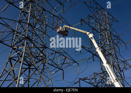 Hydro linemen on boom lift working to replace suspension insulators on high voltage electricity power line tower Stock Photo