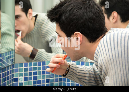 Headshot of attractive young man brushing teeth with toothbrush, looking at himself in mirror Stock Photo