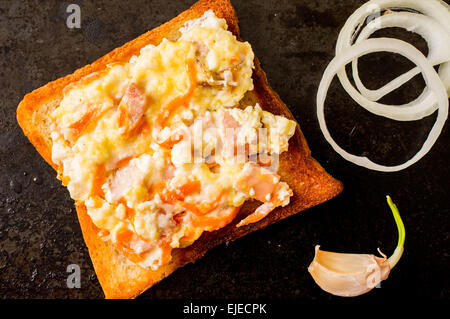 Sandwich with scrambled eggs on a black surface with onion and garlic Stock Photo