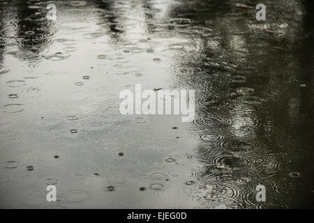 Bleak weather forecast ahead with outlook for rain as raindrops begin to fall on water surface creating ripples and splashes Stock Photo