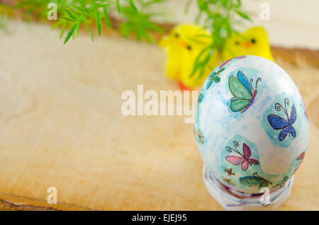 Hand painted decoupage Easter egg with small chickens and a plant in the background, placed on a wooden board Stock Photo