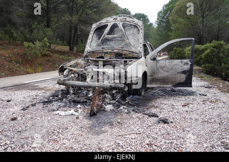 Badly abandoned burned out, burnt-out, car at side of pine forest road, Spain. Stock Photo