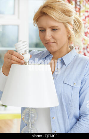Woman Putting Low Energy Lightbulb Into Lamp At Home Stock Photo