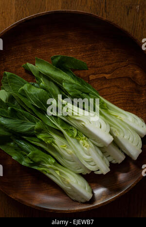 Bok choy or pak choi (Brassica rapa subsp. chinensis) sliced in quarters and ready to cook on a wooden plate. Stock Photo