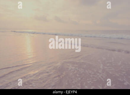 Waves on a beach. In the foreground a thin frothy wave recedes over the sand. Sun reflects on sea. Stock Photo