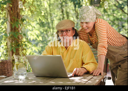Senior couple outdoors with a laptop, They're looking at the computer. Possibly having a wireless video call with grandchildren. Stock Photo