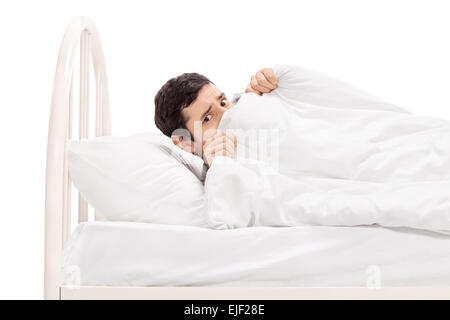 Studio shot of a scared young man hiding under a blanket and lying in bed isolated on white background Stock Photo