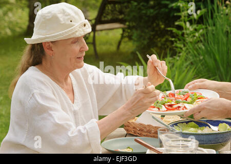 Senior woman takes a helping of salad from a plate served by a man's hands. Digital filters used. Stock Photo